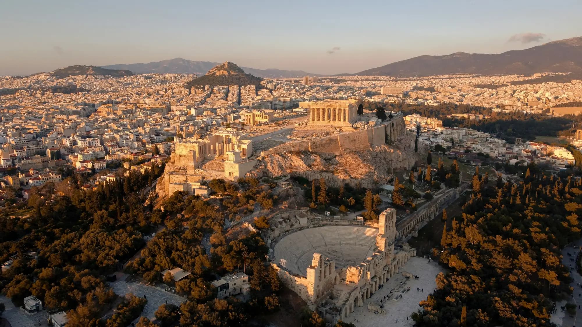 Athens seen from above at golden hour, the Acropolis rising above the city and the mountains beyond